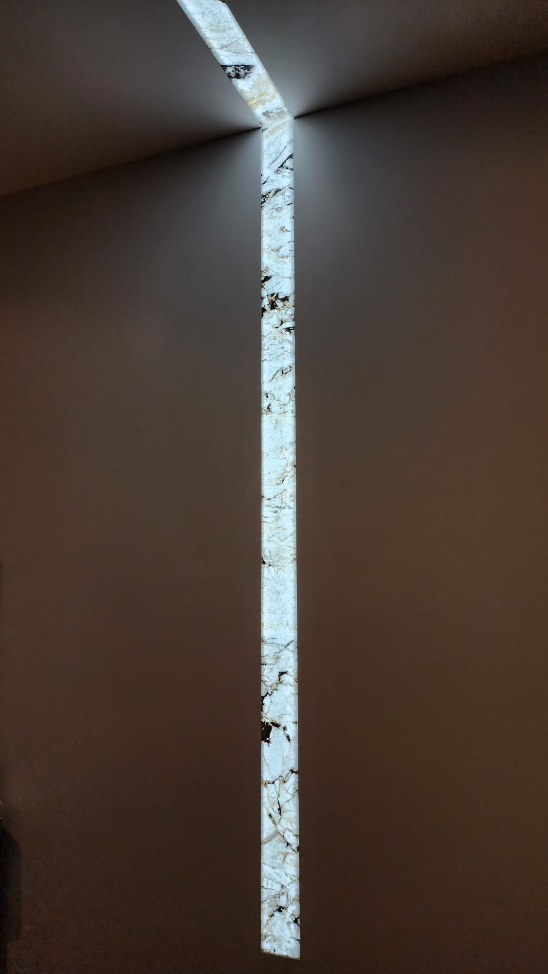 Backlit natural stone strip: wall to ceiling continuous reveal